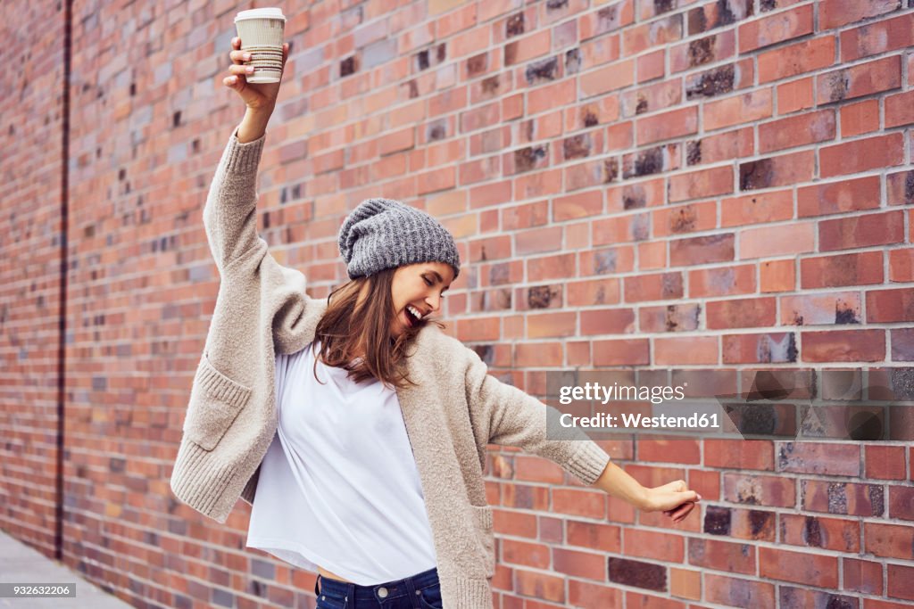 Happy woman with coffee to go singing and dancing on the street