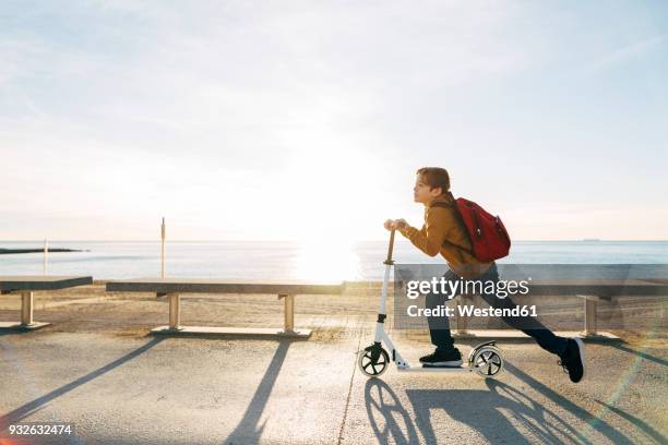 boy riding scooter on beach promenade at sunset - trotinete imagens e fotografias de stock