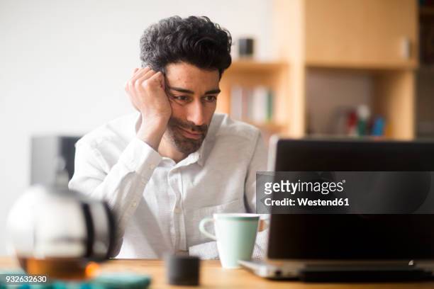 portrait of businessman at desk looking at laptop - frustration stock-fotos und bilder