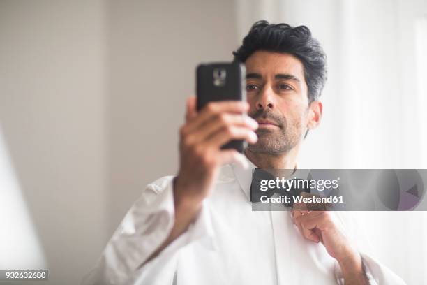 portrait of man using cell phone for adjusting his bow tie - papillon accessorio da portare al collo foto e immagini stock