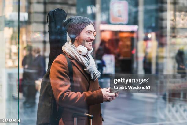 smiling young man with guitar case and cell phone - guitar case fotografías e imágenes de stock