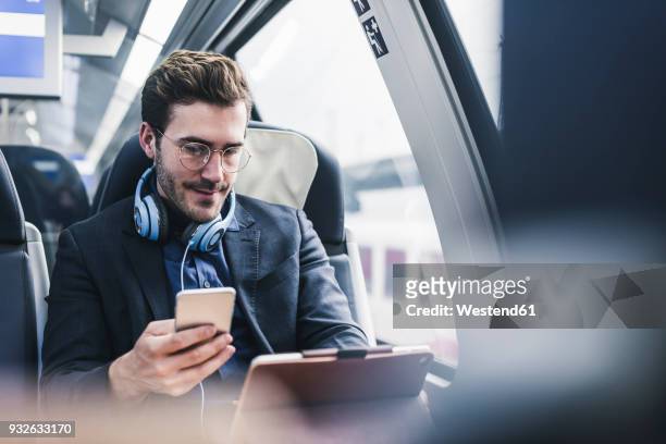 businessman in train with cell phone, headphones and tablet - journey stock-fotos und bilder