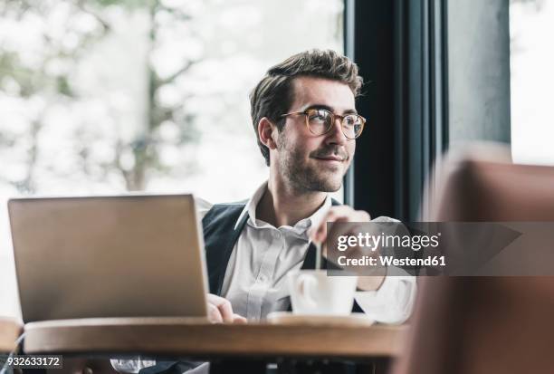 smiling young man in a cafe with laptop and cup of coffee - businessman working on a laptop with a coffee stock pictures, royalty-free photos & images