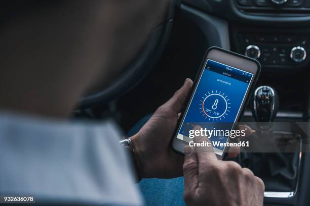 man in car adjusting smart home device via smartphone - man holding phone imagens e fotografias de stock