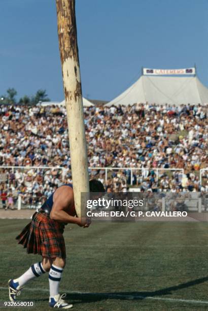 Athlete wearing a kilt carrying a caber during the Highland games, Cowal Highland Gathering, Dunoon, Scotland, United Kingdom.