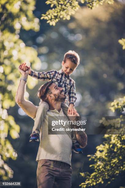 young carefree father having fun while carrying his small son on shoulders in nature. - father and son park stock pictures, royalty-free photos & images