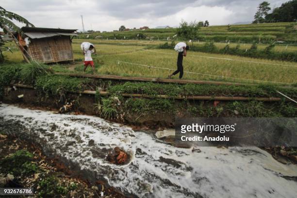 Residents carry agricultural products beside a stream of tributaries filled with textile waste in Sukamaju, Majalaya, Bandung, West Java, Indonesia,...