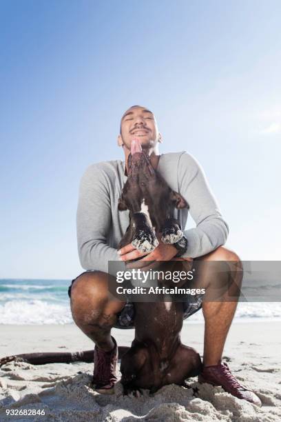 young man and his dog cuddling at the beach. - african pit bull stock pictures, royalty-free photos & images