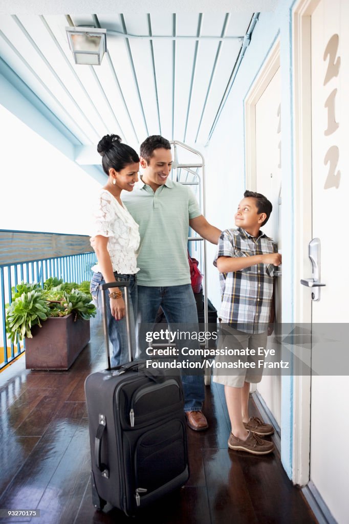 Young Family with suitcases, opening hotel door.