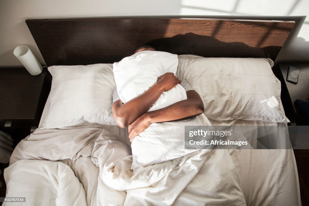 Businessman cuddling his pillow before getting out of bed for work in the morning.