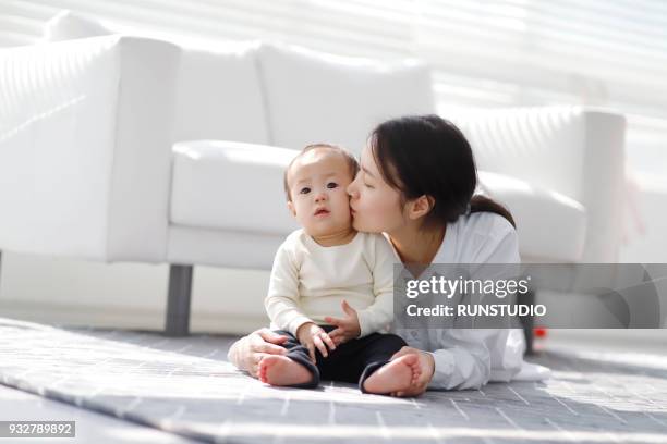 mother kissing baby cheek in living room - asian mom kid kiss stock-fotos und bilder