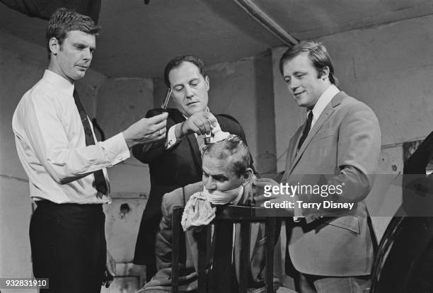 Canadian actor John Sterland has his hair shaved by actors James Fox, Stanley Meadows, and John Bindon on the set of British crime drama film...