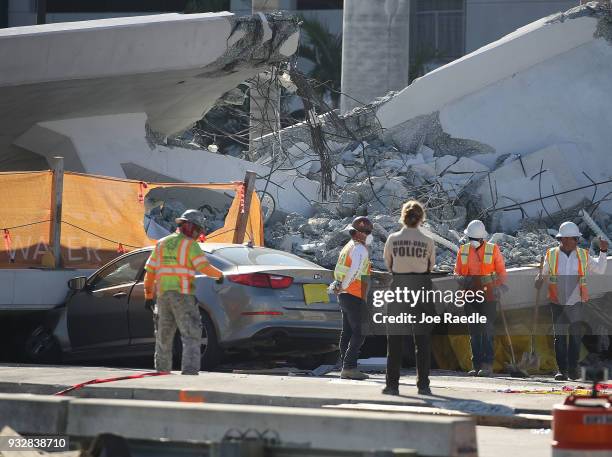 Workers, law enforcement and members of the National Transportation Safety Board investigate the scene where a pedestrian bridge collapsed a few days...