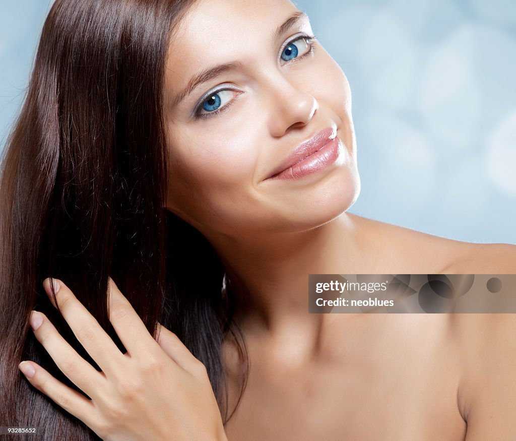 Beautiful blue-eyed woman hand brushing her long brown hair