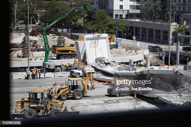 Law enforcement and members of the National Transportation Safety Board investigate the scene where a pedestrian bridge collapsed a few days after it...