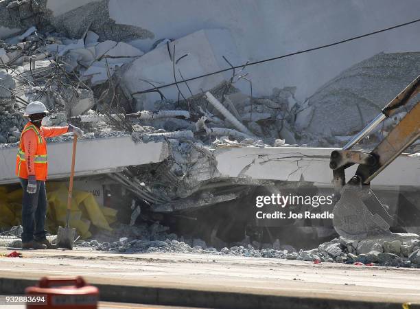 Crushed vehicle is seen near a worker as law enforcement and members of the National Transportation Safety Board investigate the scene where a...