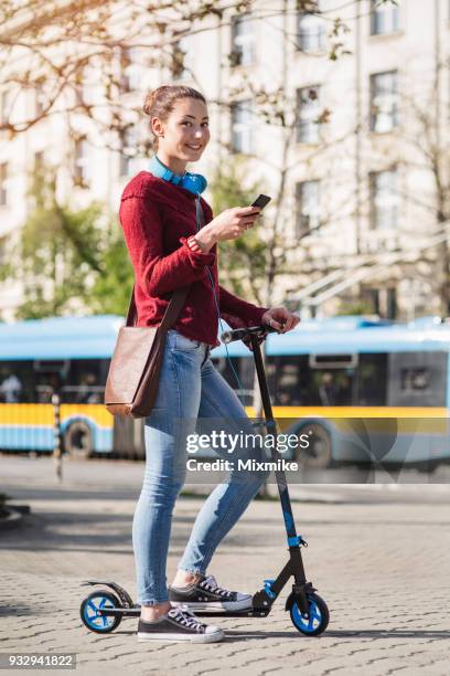 gelukkig jonge vrouw op straat met haar scooter en sms op de telefoon - 2017 common good forum stockfoto's en -beelden