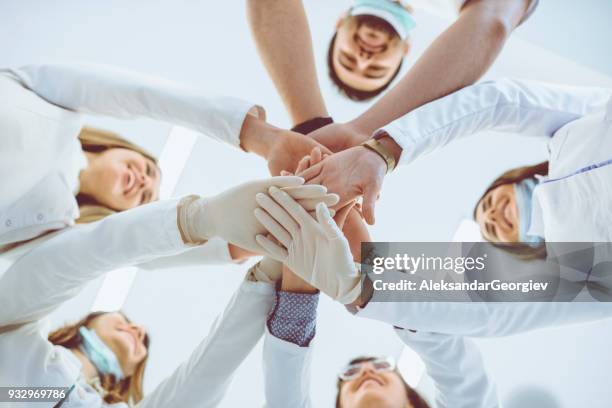 multiethnische ärzteteam stapeln hände im kreis für den erfolg - zahnarztpraxis stock-fotos und bilder