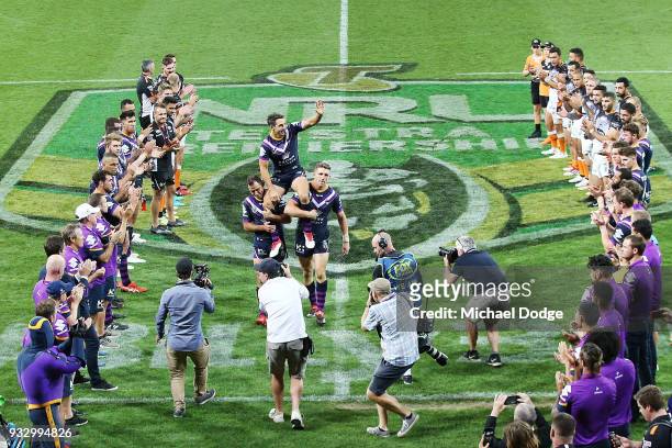 Billy Slater is carried off by Cameron Smith and Ryan Hoffman of the Storm after playing his 300th match during the round two NRL match between the...