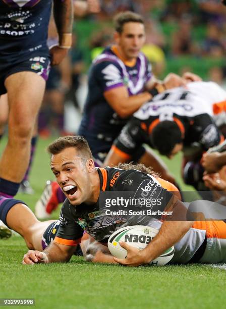 Luke Brooks of the Tigers scores the winning try as Billy Slater of the Melbourne Storm looks on behind during the round two NRL match between the...