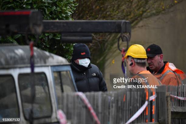 Police officer talks to vehicle recovery workers as they work to remove a vehicle from a driveway leading to the rear of the home where Russian exile...