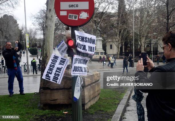 People take pictures of placards used by demonstrators in Madrid on March 17 during a protest called by the main Spanish unions and the 'State...