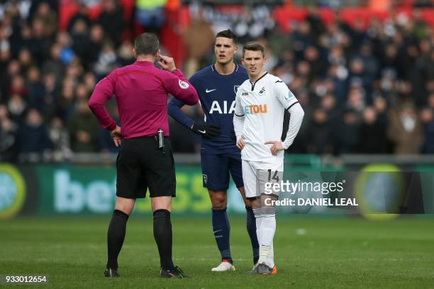 Tottenham Hotspur's Argentinian midfielder Erik Lamela and Swansea City's English midfielder Tom Carroll wait for the decision of the referee during...