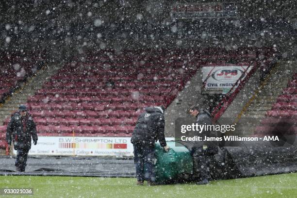 Snow falls as the Scunthorpe United groundstaff remove the pitch covers during the Sky Bet League One match between Scunthorpe United and Shrewsbury...