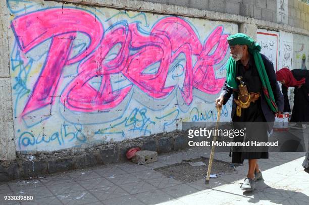 Yemeni elderly man wears ttaditional clotges walks by graffiti drew during a graffiti open day campaigning peace on March 15, 2018 in Sana'a, Yemen.