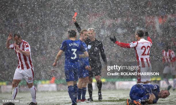 Referee Martin Atkinson awards Stoke City's Scottish midfielder Charlie Adam a red card as Everton's English striker Wayne Rooney clutches his leg...