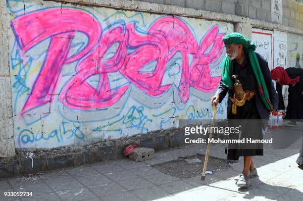 Yemeni elderly man wears ttaditional clotges walks by graffiti drew during an Open Day of graffiti campaign call for peace on March 15, 2018 in...