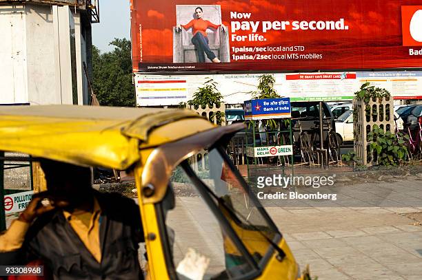 An auto rickshaw driver stops under a billboard advertising reduced rates for the mobile phone provider MTS, a brand of Sistema Shyam TeleServices...