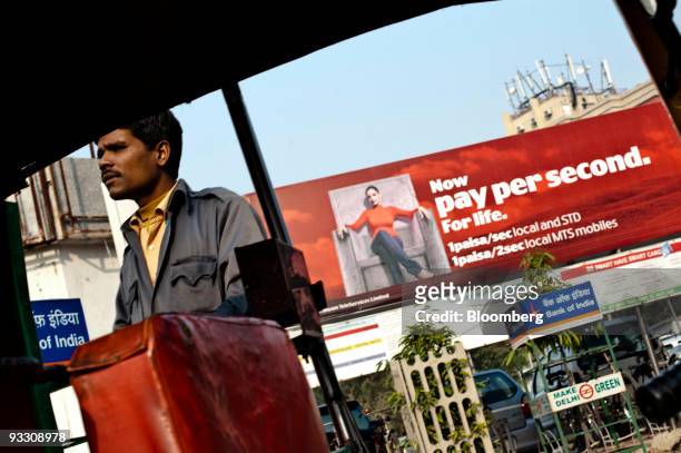 An auto rickshaw driver stands under a billboard advertising reduced rates for the mobile phone provider MTS, a brand of Sistema Shyam TeleServices...