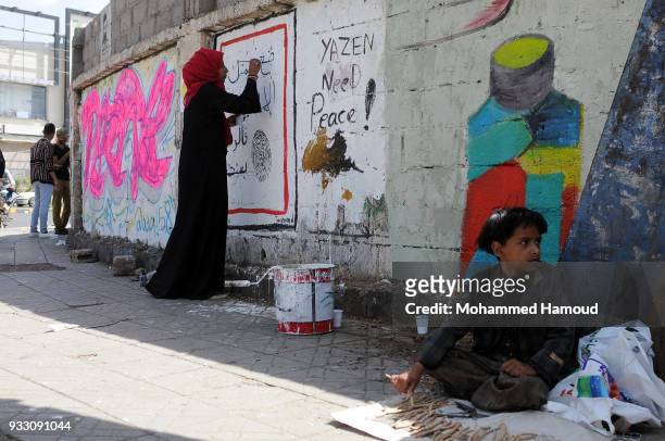 Child sells wood toothpick as he sits on a pavement as artists draw graffiti during an Open Day of graffiti campaign call for peace on March 15, 2018...
