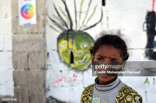 Little girl stands in ftont of graffiti drew during an Open Day of graffiti campaign call for peace on March 15, 2018 in Sana'a, Yemen.