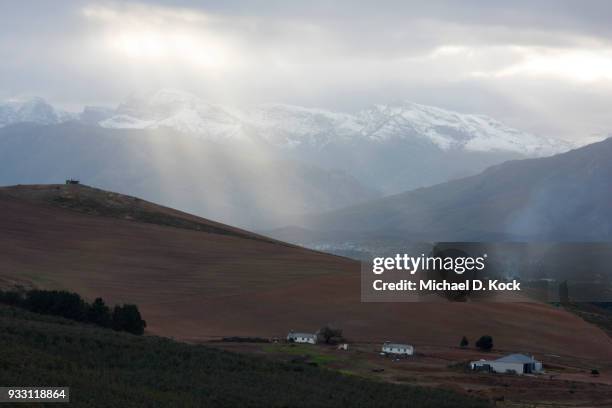 oewerzicht farm in the foreground with the village of greyton in the distance, snow on mountains with sunlight piercing the clouds, overberg, western cape - overberg stock pictures, royalty-free photos & images