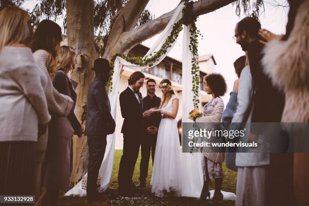 braut und bräutigam den austausch von trauringe bei zeremonie mit gästen - beistand des bräutigams stock-fotos und bilder