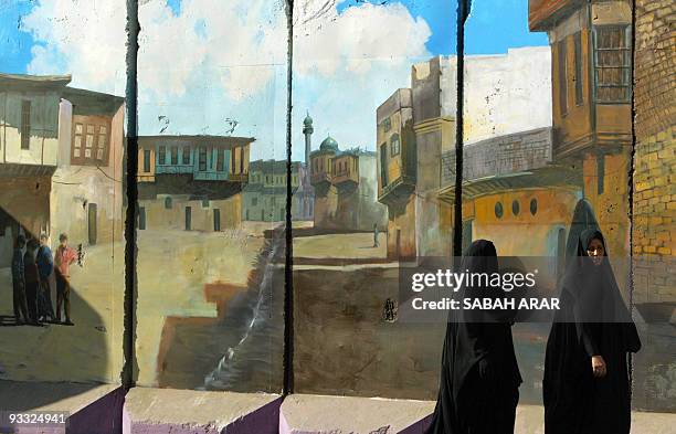 Iraqi women walk past cement wall decorated with a mural depicting a scene of an old Baghdad neighborhood, 04 October 2007 in central Baghdad. The...