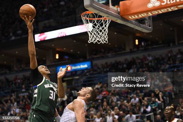 John Henson of the Milwaukee Bucks shoots over Mike Muscala of the Atlanta Hawks during the second half of a game at the Bradley Center on March 17,...