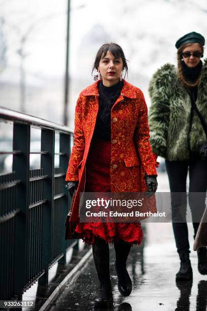 Guest wears large earrings, a black top, an orange brocade coat with yellow pattern, a red lace trumpet dress, black gloves, black patent shoes,...