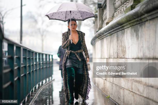 Guest holds a white umbrella and wears a black V-neck top, a marled brown fringe maxi coat, dark emerald green over-knee boots, outside Balmain,...