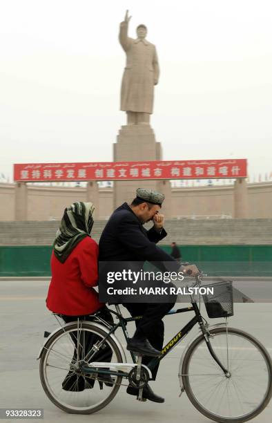 Chinese Muslim Uighur couple rides past a statue of the late Chinese leader Mao Zedong in the town of Kashgar, Xinjiang Province on April 2, 2008....