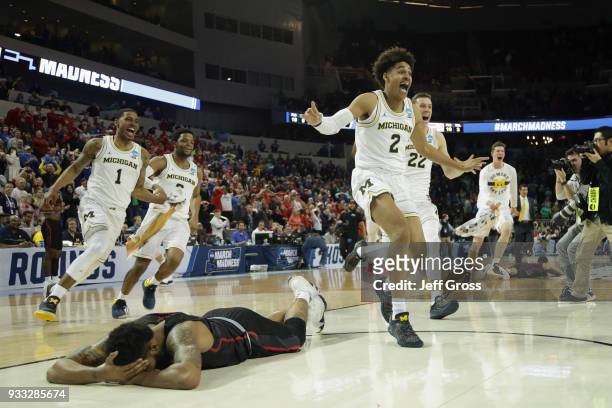 Jordan Poole and teammates of the Michigan Wolverines celebrate Poole's 3-point buzzer beater for a 64-63 win as Devin Davis of the Houston Cougars...
