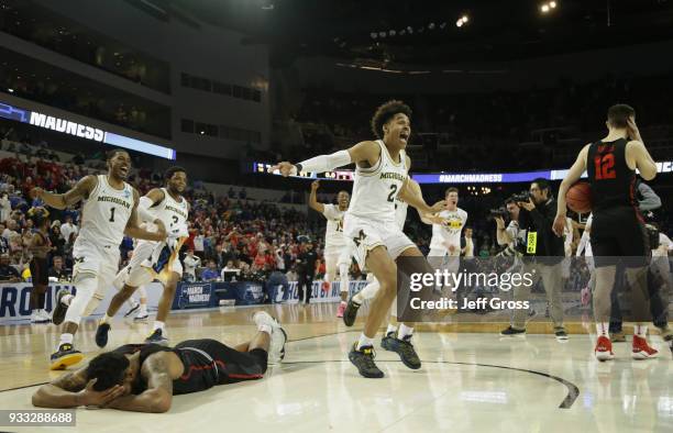 Jordan Poole and teammates of the Michigan Wolverines celebrate Poole's 3-point buzzer beater for a 64-63 win as Devin Davis of the Houston Cougars...