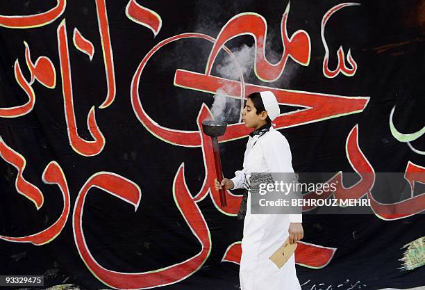 An Iranian boy blows the insence as he walks past a religious banner in the Khomeini Shahr suburb of the central Iranian city of Isfahan during a...