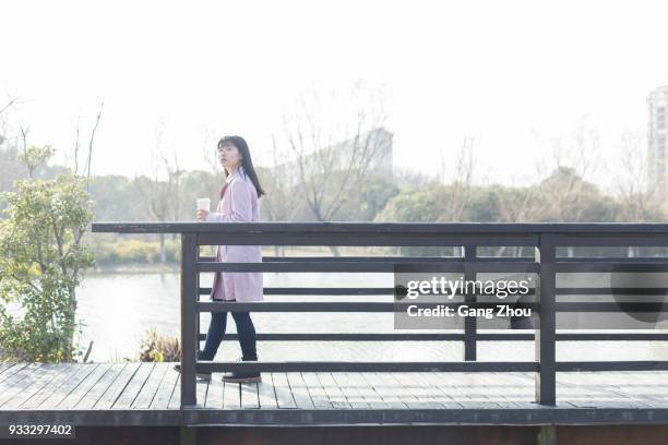 side view of young female holding disposable cup walking on bridge - bridge side view stock pictures, royalty-free photos & images