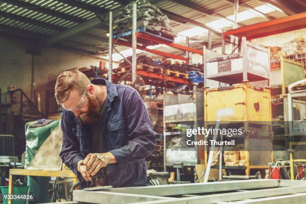 jonge metal werknemer met machtshulpmiddel in fabriek met beschermende uitrusting - metal sanding stockfoto's en -beelden