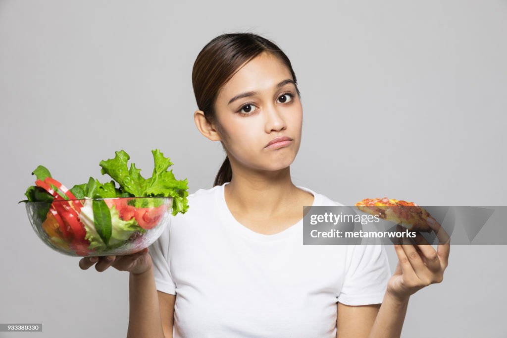 Young woman holding salad bowl and pizza.