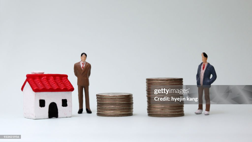 Zwei Miniatur-Männer stehen neben einem Haufen von Münzen und Miniaturhaus.