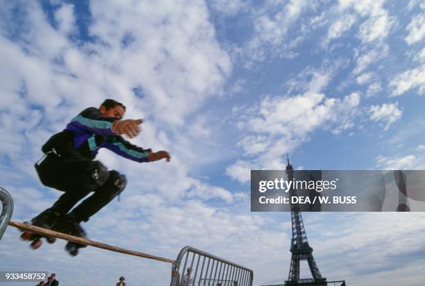 Boy wearing roller skates jumping a hurdle, with the Eiffel Tower in the background, Jardins du Trocadero, Paris, France.